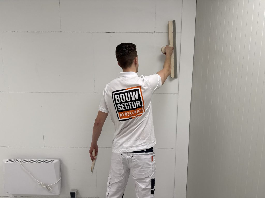 Stukadoor van Bouwsector Nederland zet een lange spaan tegen een gipsplaatwand met nog zichtbare naden