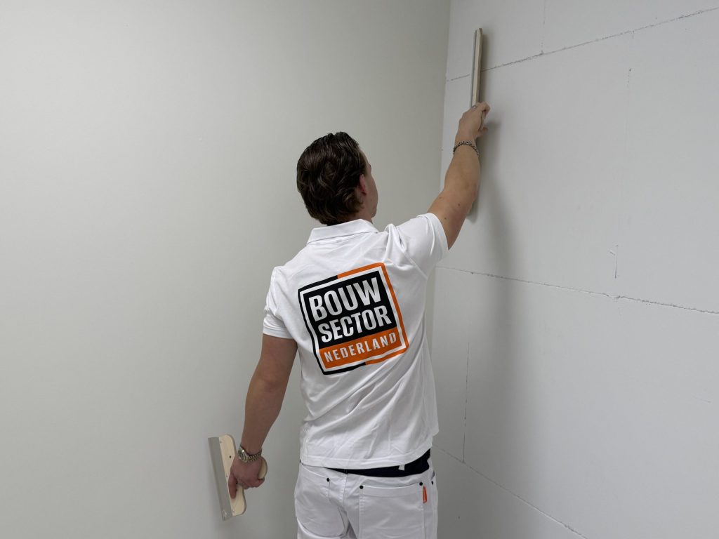 Stukadoor van Bouwsector Nederland trekt met een lange spaan de wand vlak bij de hoek van de kamer