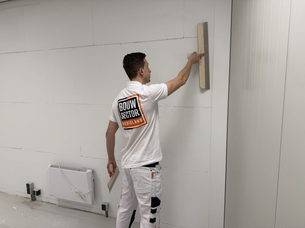 Stukadoor trekt met een brede spaan de pleister vlak op een wand boven een elektrische kachel
