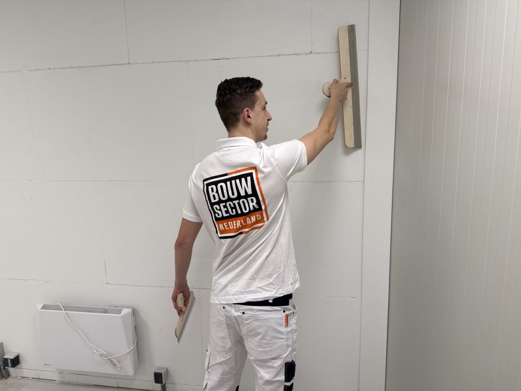 Stukadoor van Bouwsector Nederland zet een brede spaan hoog op een binnenwand
