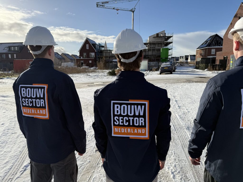 Drie vakmensen van Bouwsector Nederland met witte helm kijken naar nieuwe woningen in de sneeuw